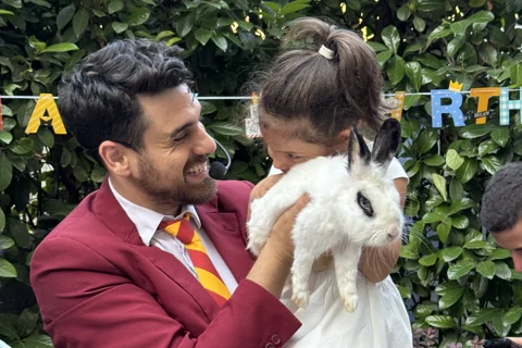 Mago Max in giacca rossa con sciarpa Grifondoro e bambina con coniglietto bianco
