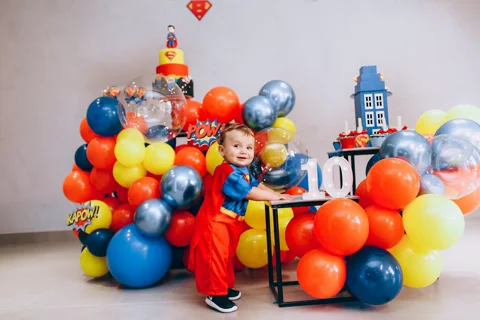 Bambino in costume Superman a festa supereroi con palloncini POW