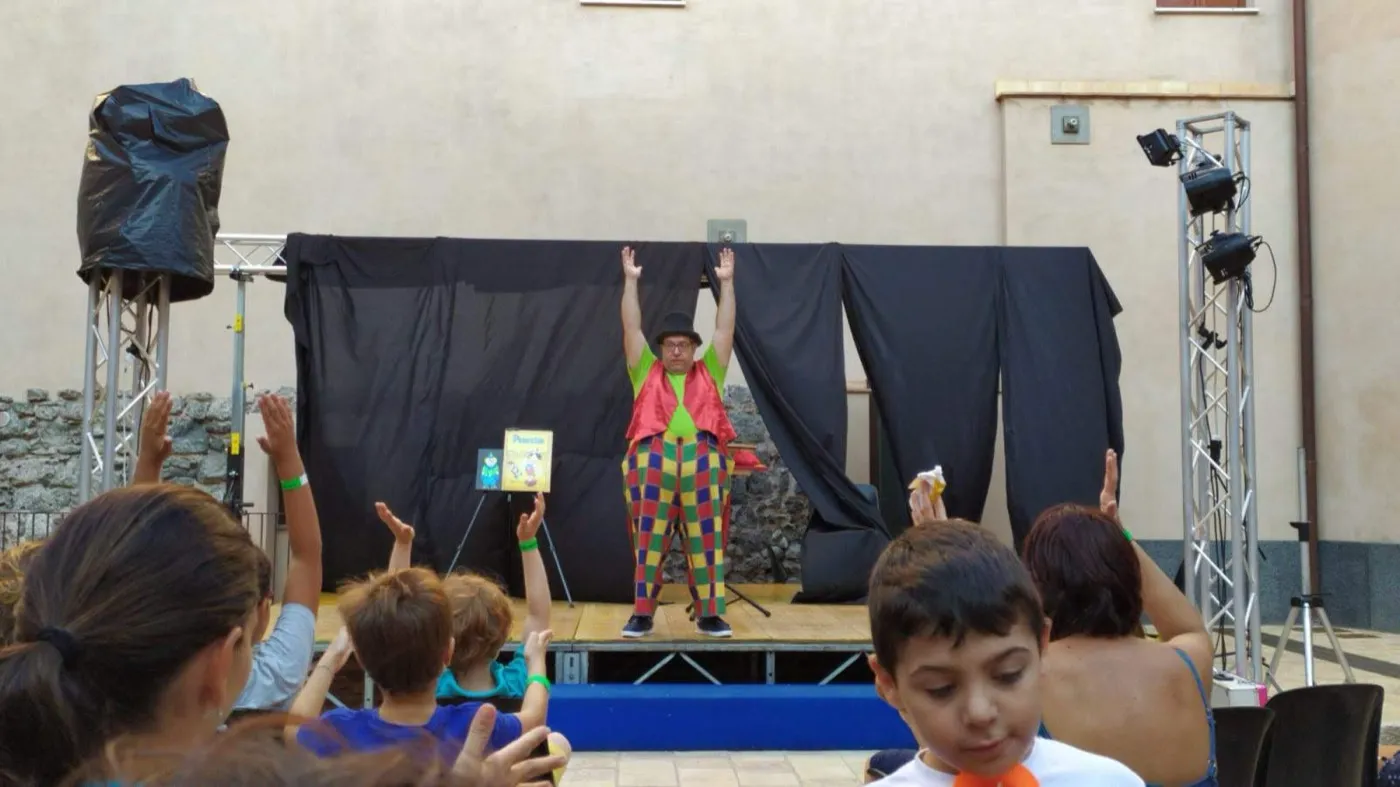 Bambini che alzano la mano per partecipare allo spettacolo sul palco all'aperto