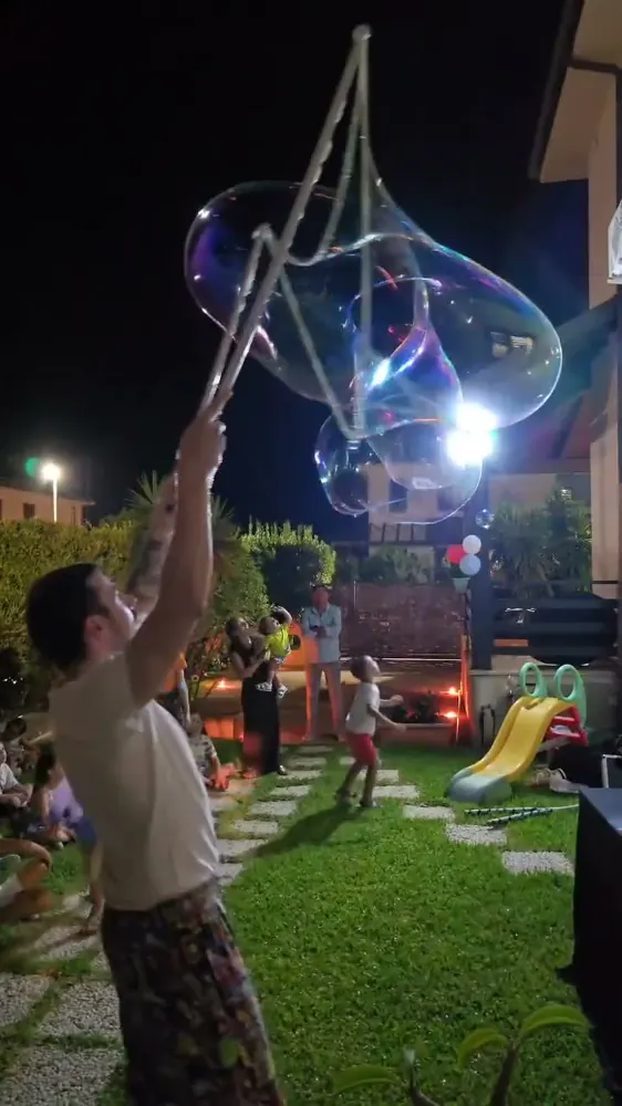 Animatore con una gigantesca bolla di sapone luminosa nel giardino di una festa, di sera