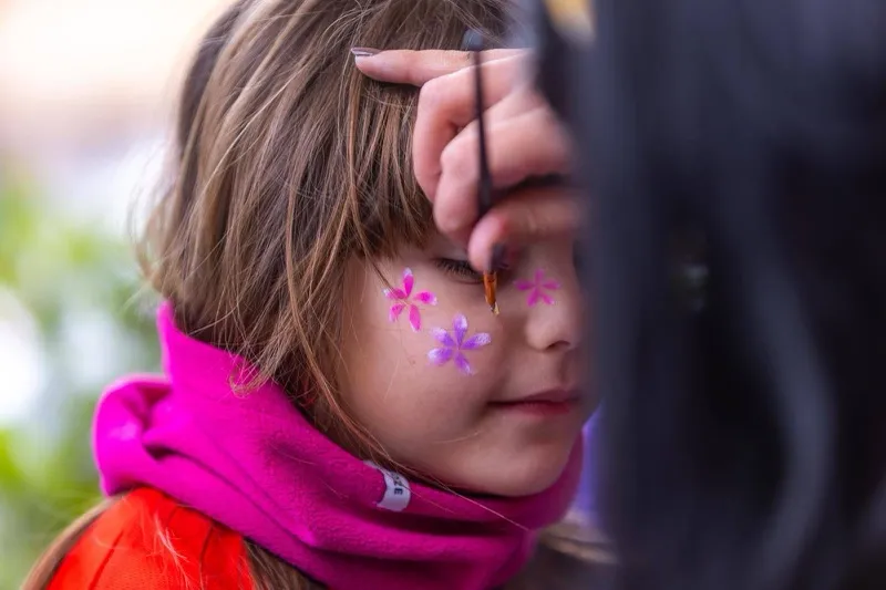 Animatrice che dipinge farfalle e fiori sul viso di una bambina