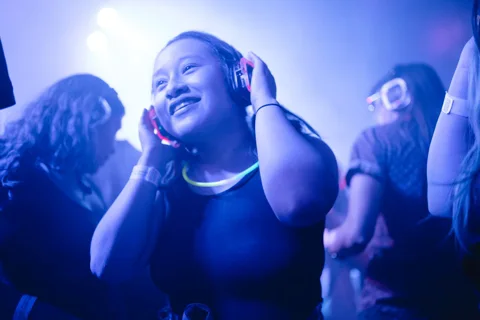 Donna con cuffie luminose blu balla in silent disco club