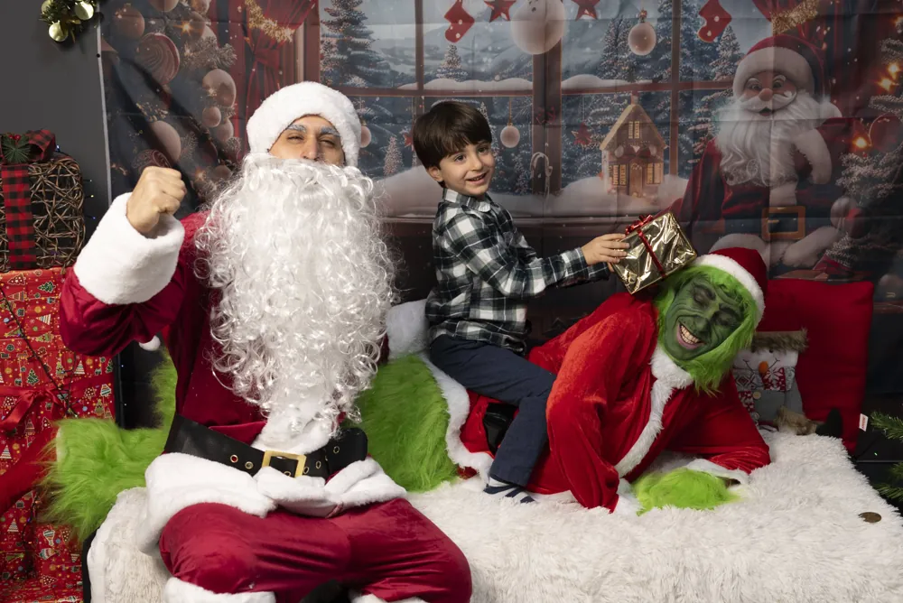 Un bambino gioca con Babbo Natale mentre il Grinch sbircia