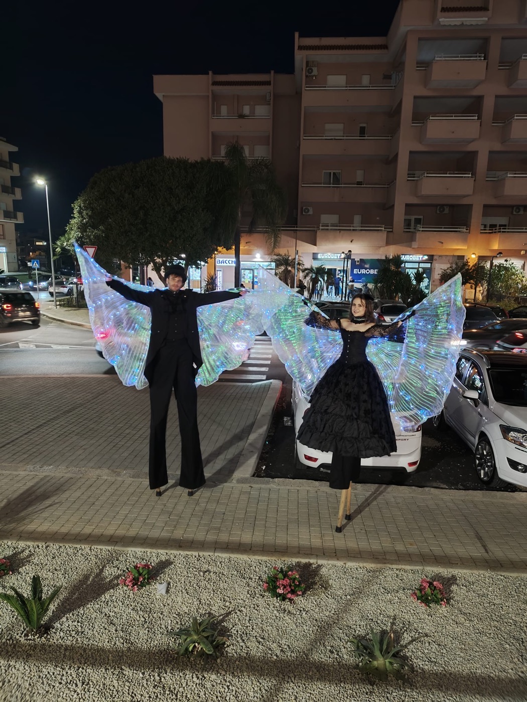 Coppia trampolieri con ali LED a farfalla luminose multicolore in evento serale notturno